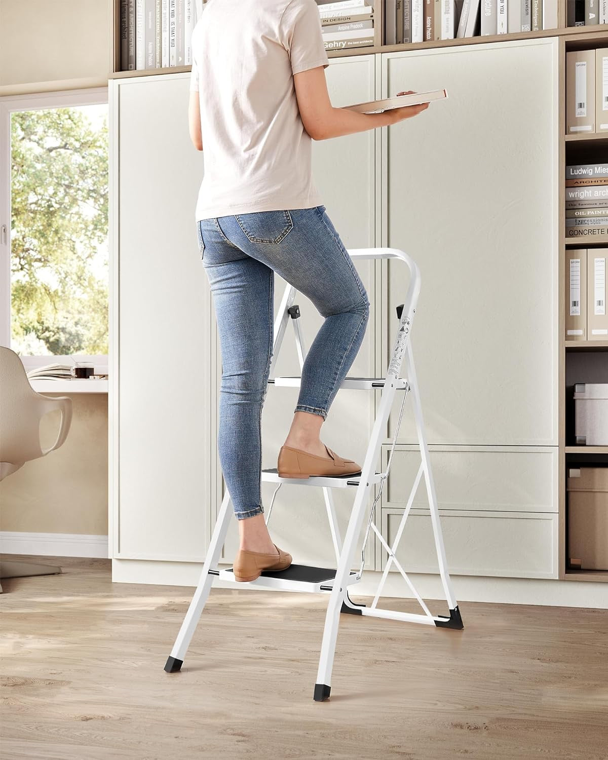 Woman using a 3-step folding ladder in a modern kitchen to reach high shelves safely.